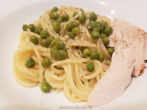 A piece of rotisserie chicken, served on the side of lemon pasta and peas.