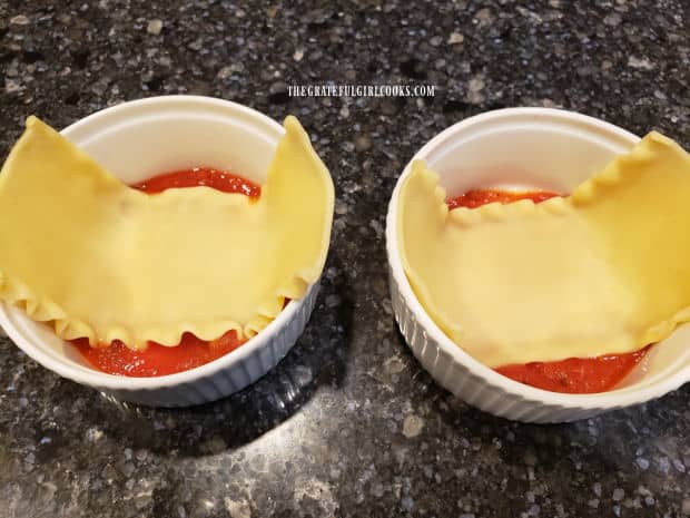 Mini lasagna bowls begin with a layer of marinara sauce, topped with a cooked lasagna noodle.