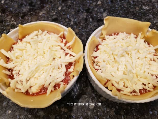 Grated cheese is added to each of the mini lasagna bowls in layers.