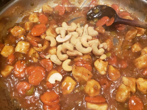 Roasted cashews are added to the thick orange sauce, chicken and veggies in skillet.