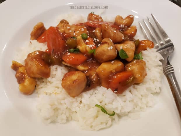 Orange Cashew Chicken is served on white rice, garnished with green onions and sesame seeds.