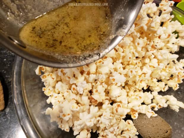 Seasoned butter is drizzled over popped popcorn and stirred to combine.