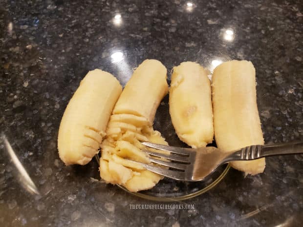 Bananas are being mashed using the backside of a fork.