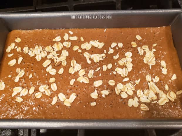 Old fashioned oats are sprinkled on top of brown bread, halfway through baking.