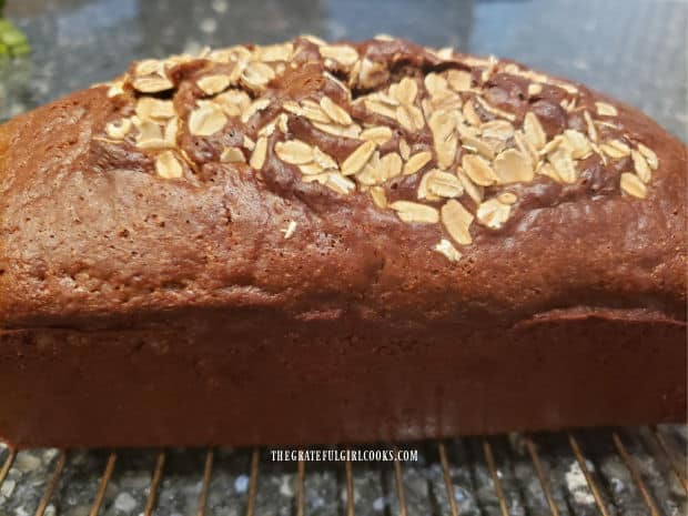 A loaf of delicious, baked brown bread, cooling on a wire rack.