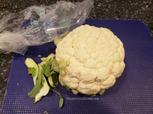 A head of cauliflower is removed from package and leaves and stems are removed.