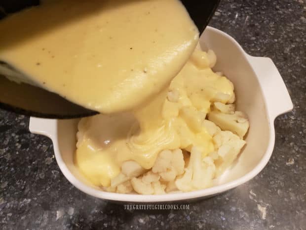 Thick creamy cheese sauce is poured over cauliflower florets in baking dish.