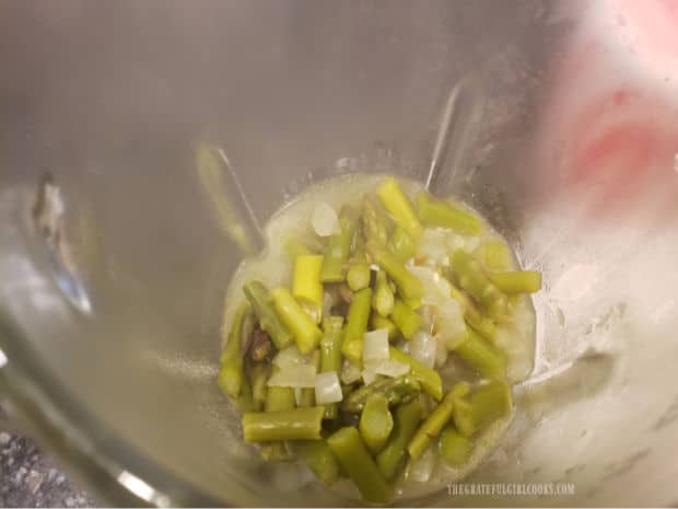 Half the soup mixture is transferred out of the saucepan into a blender for processing.