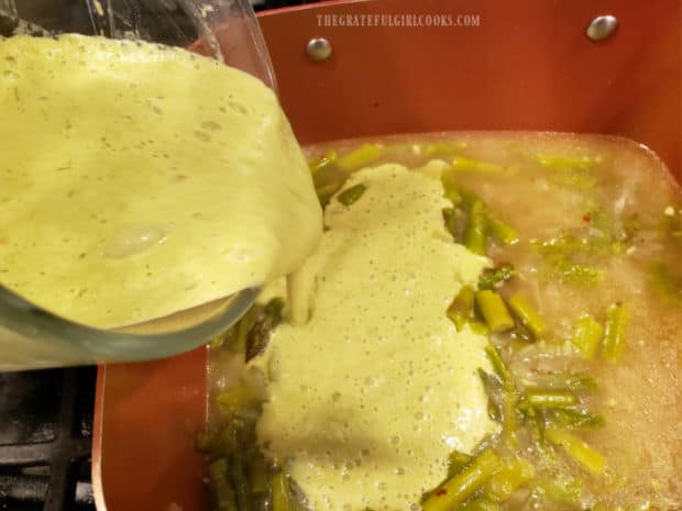Pureed cream of asparagus soup is added back into remaining ingredients in saucepan.