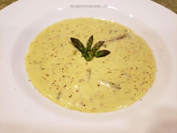 The cream of asparagus soup is sprinkled with ground nutmeg and served hot, in a white bowl.