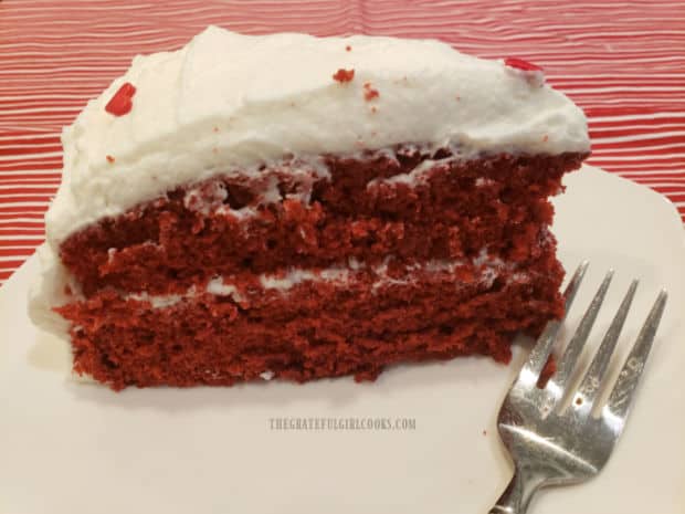 A slice of Grandma's red velvet cake ready to eat, on a white plate.
