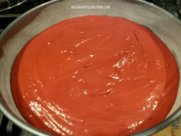 Greased/floured cake pans are filled with batter for the red velvet cake, and put in oven to bake.