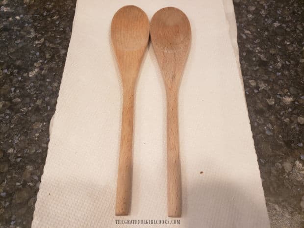 Two wooden spoons are placed side by side to assist in slicing Hasselback potatoes.