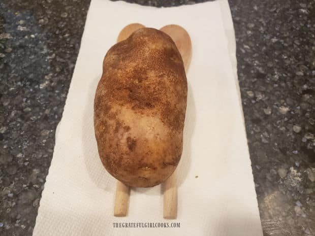 A potato is placed on top of two wooden spoons, side by side, in order to slice it.