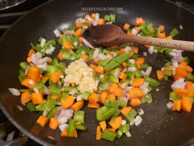Chopped green pepper, carrot, red onion, and garlic are cooked in oil until tender.