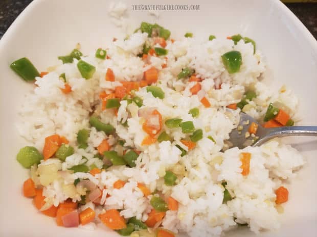 The cooked veggies are added to the cooled rice in salad bowl.