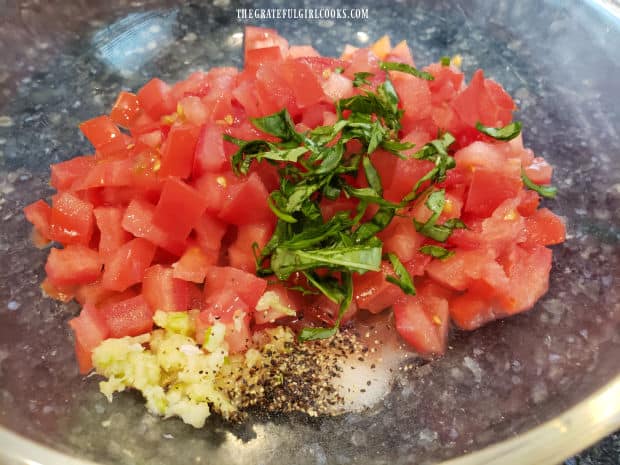 Chopped tomatoes, basil, garlic and spices are combined in a bowl.