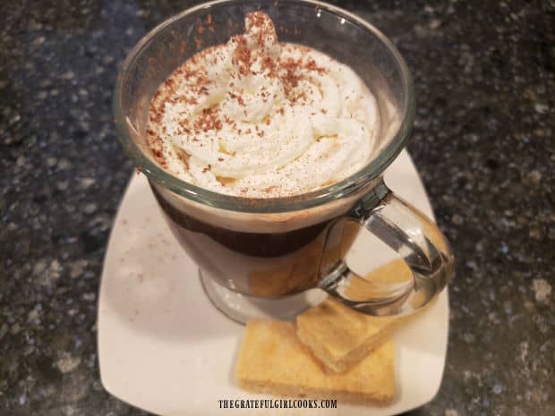 A mug of hot cinnamon mocha coffee is served, topped with whipped cream and cinnamon.