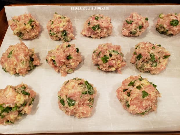 Twelve meatballs are placed on a parchment paper-lined baking sheet to bake.