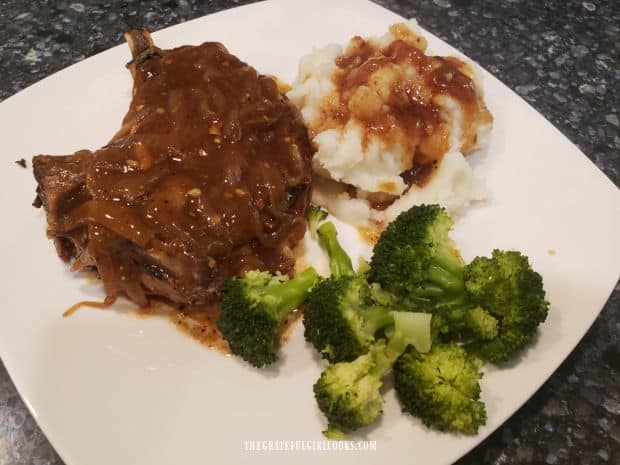 A serving of smoked smothered pork chops, with mashed potatoes and broccoli on the side.