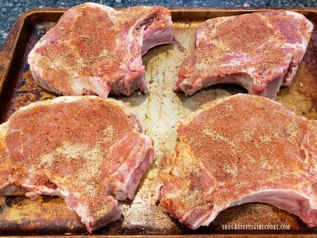 Four bone-in pork chops are coated with spices on both sides before cooking.