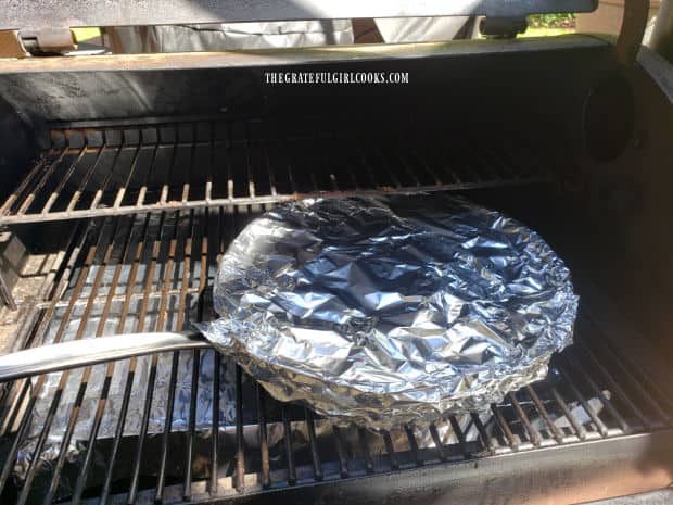 Smoked smothered pork chops are cooked on a Traeger grill in a foil-covered skillet.