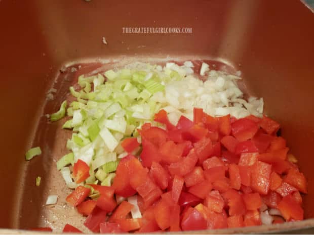 Chopped onion, red bell peppers and celery are cooked until softened in saucepan.