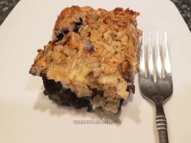 Slice of blueberry banana baked oatmeal, served on a white plate with a fork.