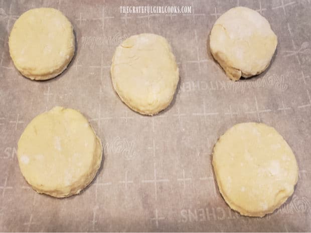 Five biscuits on a parchment paper lined baking sheet, ready to bake.