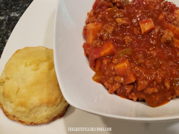 One of the buttery biscuits, ready to enjoy eating, alongside a bowl of chili.