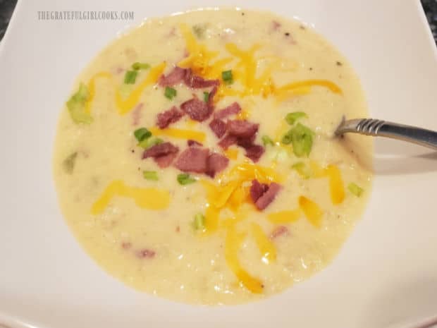 Bowl of cauliflower bacon chowder is served, topped with green onions, cheese and bacon.