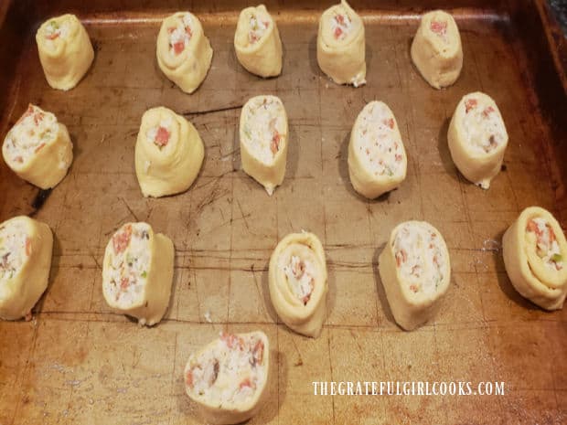 Sixteen cheesy calzone pinwheels on baking sheet, ready to bake.