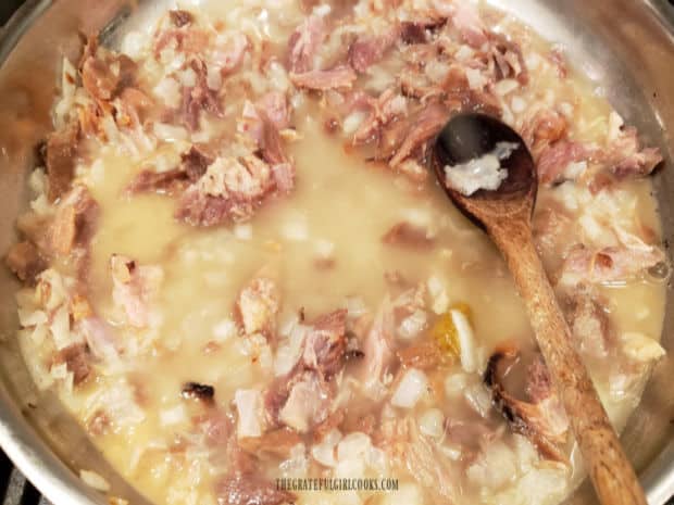 Chicken broth and water are stirred into the skillet with ham and onions.