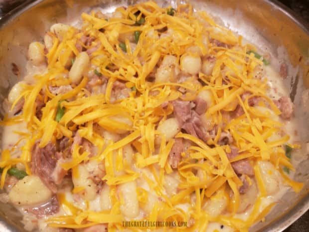 Grated cheddar cheese is added to ham and cheddar gnocchi, then skillet is put under a broiler.
