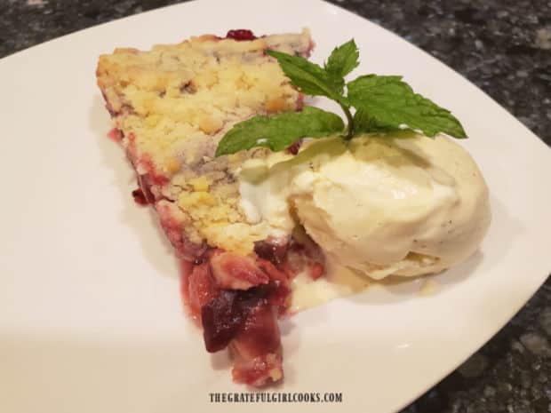 A slice of Italian plum shortbread tart, served with a scoop of vanilla ice cream & mint sprig.