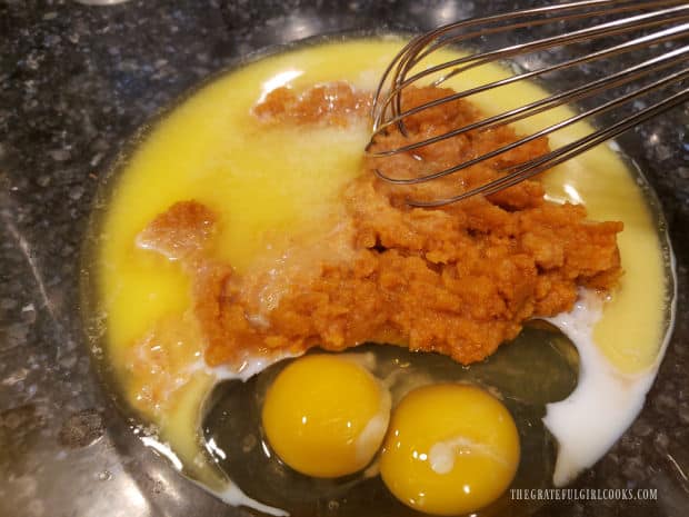 Melted butter, pumpkin puree, eggs and vanilla extract are whisked together in large glass bowl.