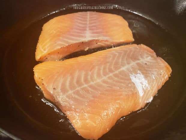 The salmon fillets are pan-seared, seasoned side down in hot oil in a skillet.