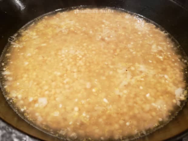 Water is added to the pearl couscous and it begins cooking in skillet.