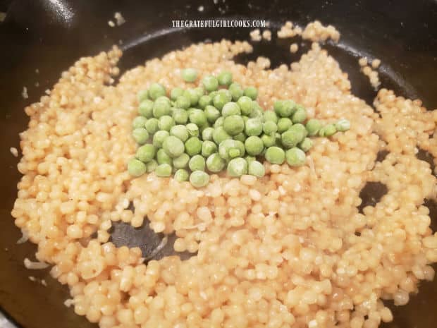 Frozen peas are added to the skillet of hot pearl couscous.