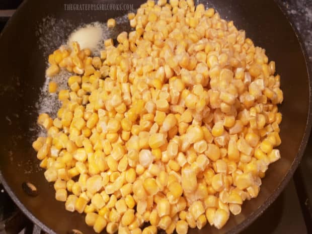 Frozen corn is added to a large skillet with melted butter in it.