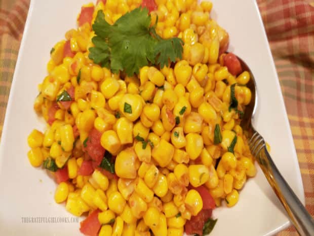 The corn is transferred to a white serving dish, and topped with cilantro leaves.