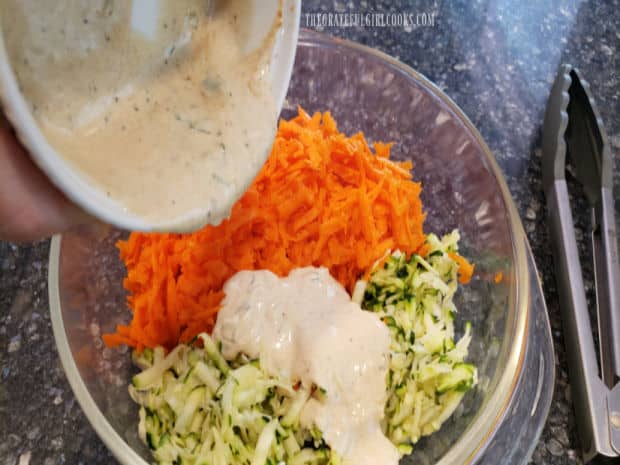 The dressing is combined with shredded zucchini and carrots in a mixing bowl.