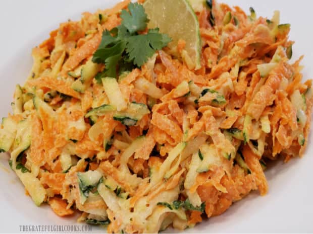 Delicious zucchini carrot lime coleslaw is served in a white bowl, with cilantro/lime garnish.