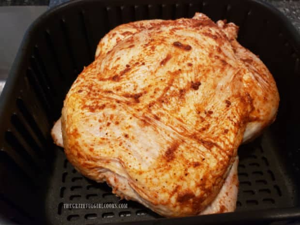 An entire seasoned chicken, before cooking, in an air fryer basket.