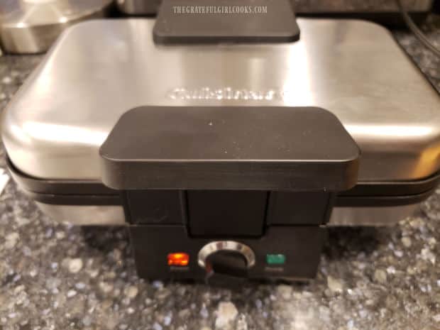 A pizzelle press being preheated before adding batter.