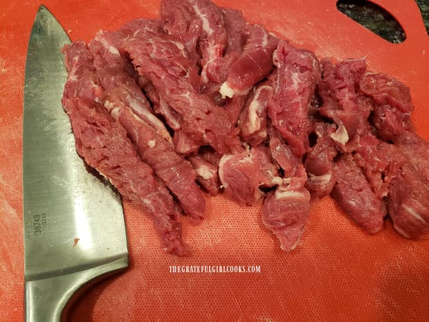 Flank steak is sliced into thin strips on a cutting mat.