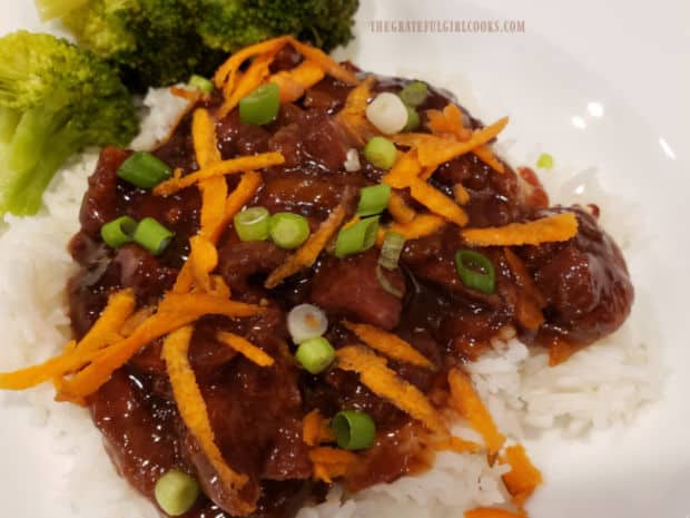 Crock pot Mongolian beef is served on rice, with a garnish of chopped green onions.