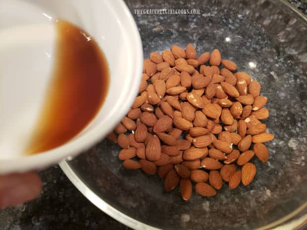 A mixture of liquid smoke and water is poured onto the unblanched almonds in a bowl.