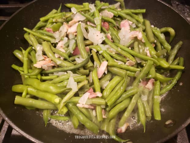The green beans and bacon are cooked in butter in a large skillet.