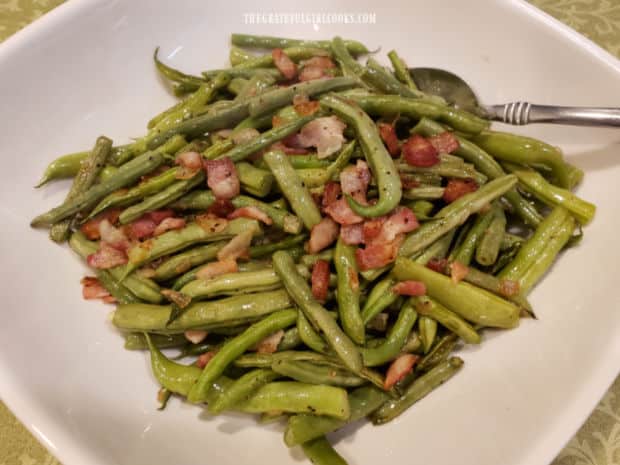 The hot green beans and bacon are served in a white serving bowl.